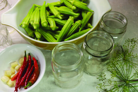 a colander of washed okra, a bowl of sliced garlic and whole chilis, three open…